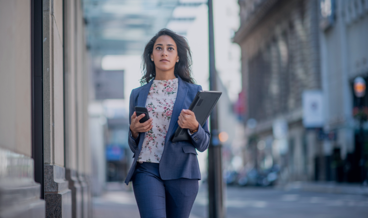 Careers at Hexafin – confident young professional walking in city holding laptop and phone, representing growth, ambition, and career opportunities in finance.